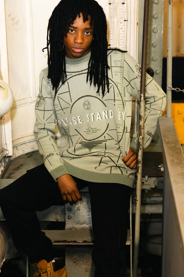 Person wearing a light green sweatshirt with text, sitting on a metal staircase.