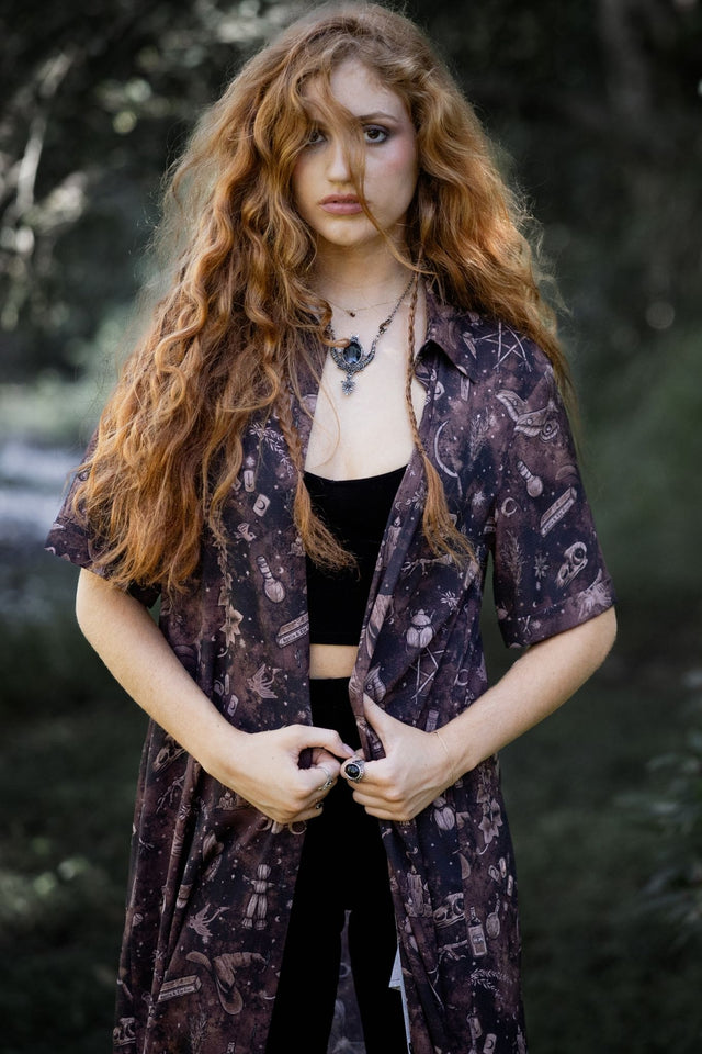 Brown witchcore midi dress with Ami Raithe artwork featuring bones, potion bottles, butterflies and mystical occult details. This alternative goth button-through dress captures cottage witch, dark fairycore and fantasy witch aesthetics from the Nature of a Witch collection.