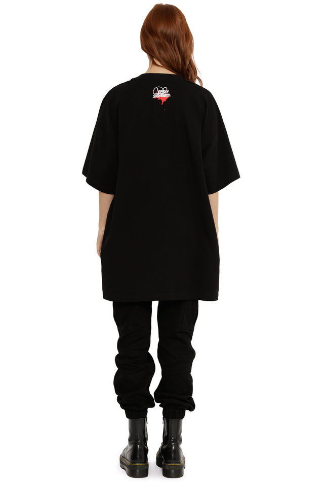 Person wearing a black oversized t-shirt with a logo on the back, standing against a white background.