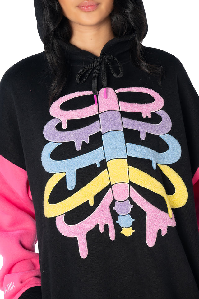 Black oversized unisex hoodie with rainbow skeleton design, contrast hot pink sleeves, embroidered logo details and soft winter fleece fabric for everyday wear.