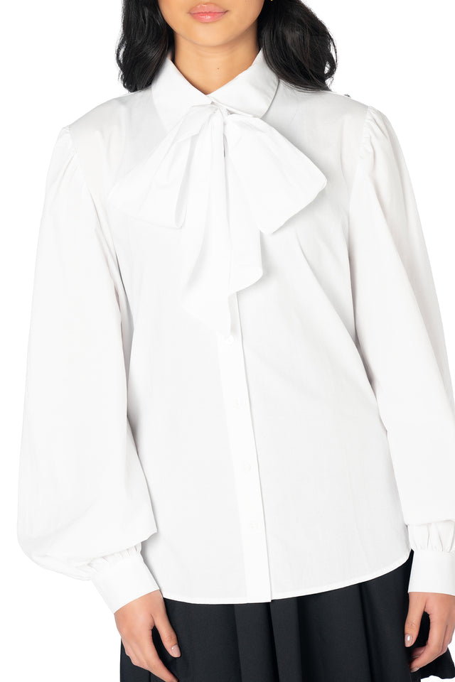 White statement shirt featuring a detachable bow neckline, voluminous sleeves and a tailored button-up silhouette, ideal for pairing with skirts, trousers and tailored shorts.