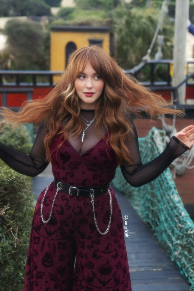 Woman in a burgundy dress with black lace overlay standing on a dock.