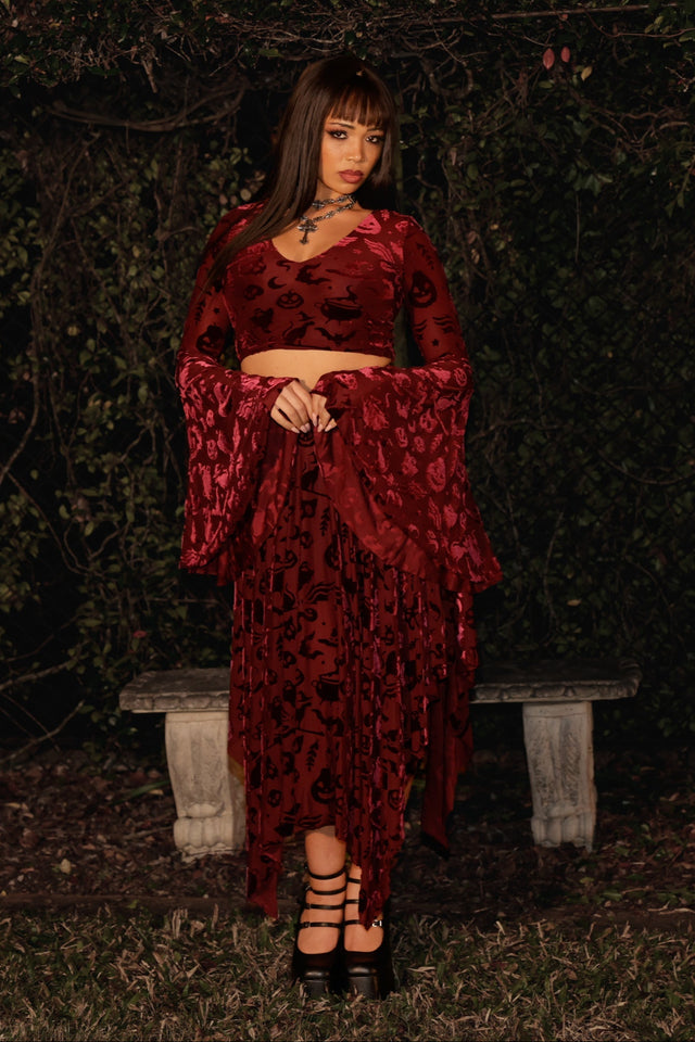 Woman in a red dress standing in a dark, outdoor setting with a bench.