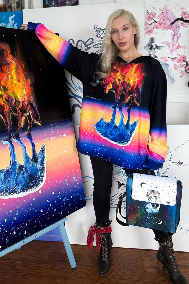 Person wearing a colorful hoodie with a design of a blue creature on fire, standing next to a painting of the same design.