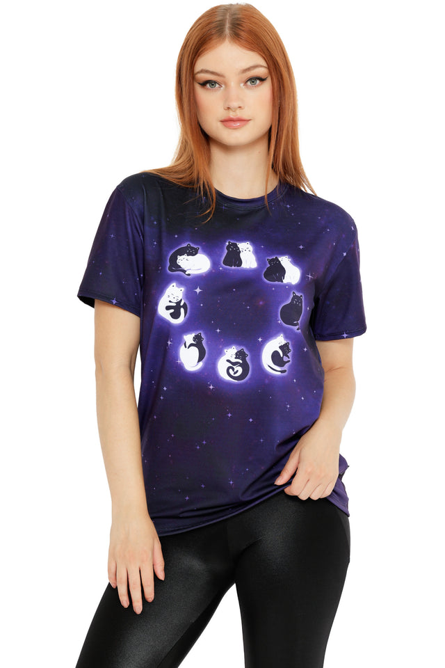 Model wearing a deep purple galaxy tee featuring glowing cats arranged in moon phase positions across the chest, paired with black leggings.