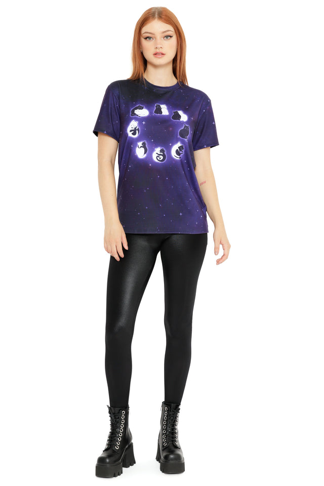 Purple space-print T-shirt with luminous black and white cats forming a circular moon phase design, styled on a model against a white background.