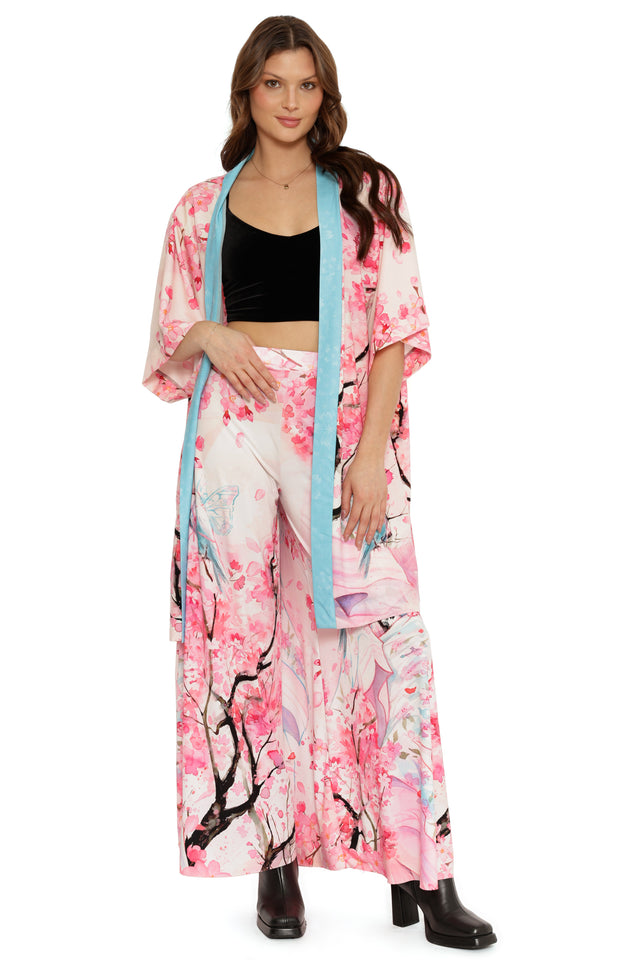 Woman wearing a pink floral kimono with a black top and white pants on a white background