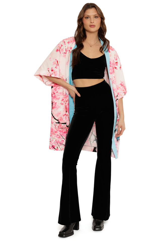Woman wearing a black outfit with a pink floral kimono over a white background