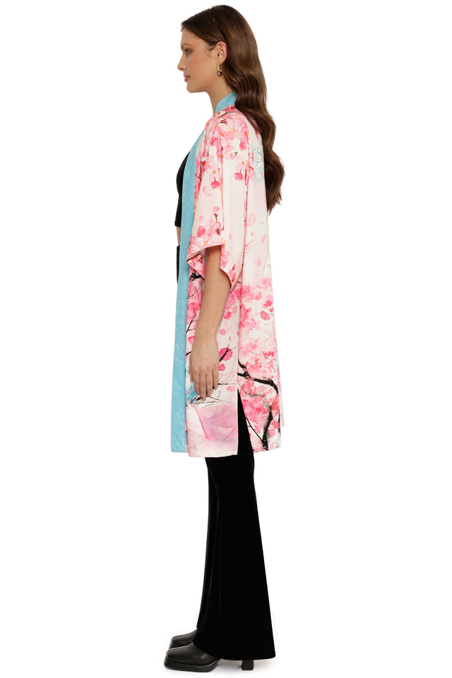 Woman wearing a pink floral kimono over a black outfit with a white background