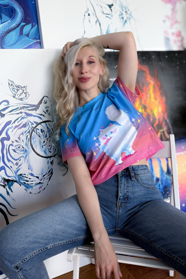 Woman wearing a colorful shirt with a graphic design, sitting in front of art pieces.