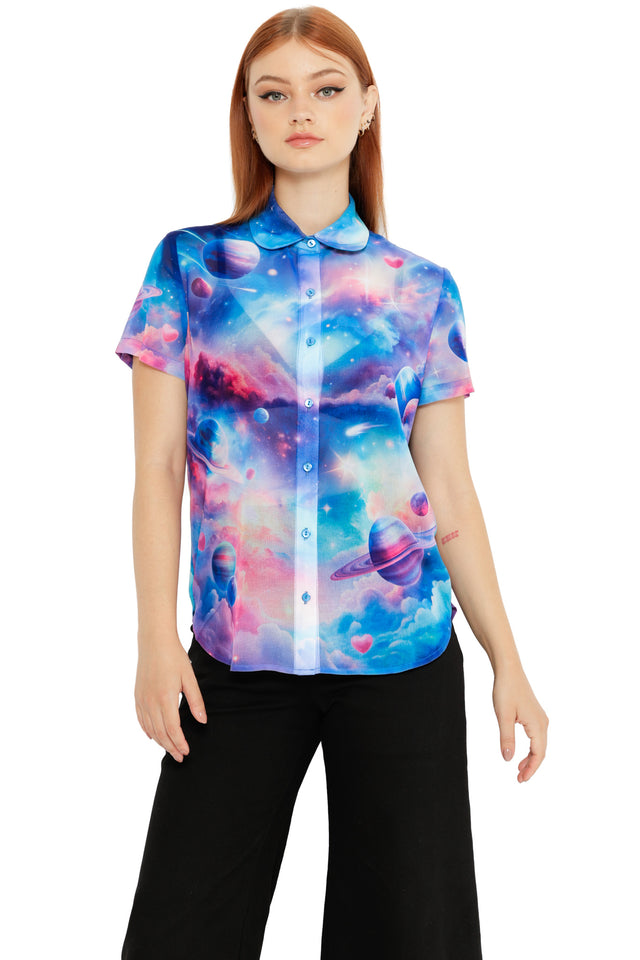 Model wearing a pastel galaxy button-up shirt with planets, clouds and pink heart details on a blue sky background.