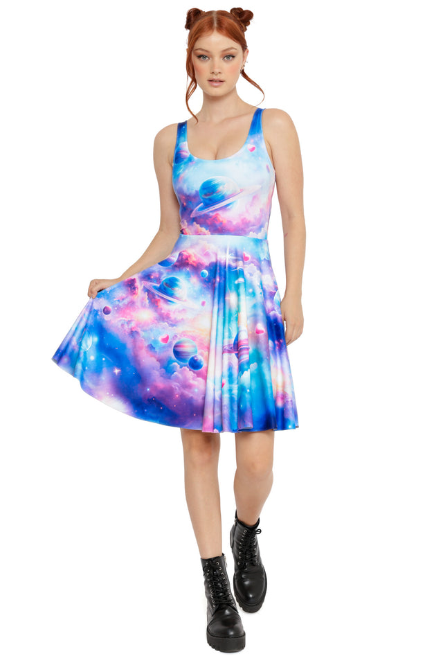 Model wearing a pastel galaxy skater dress with planets, nebula clouds and pink heart details, styled with black lace-up boots