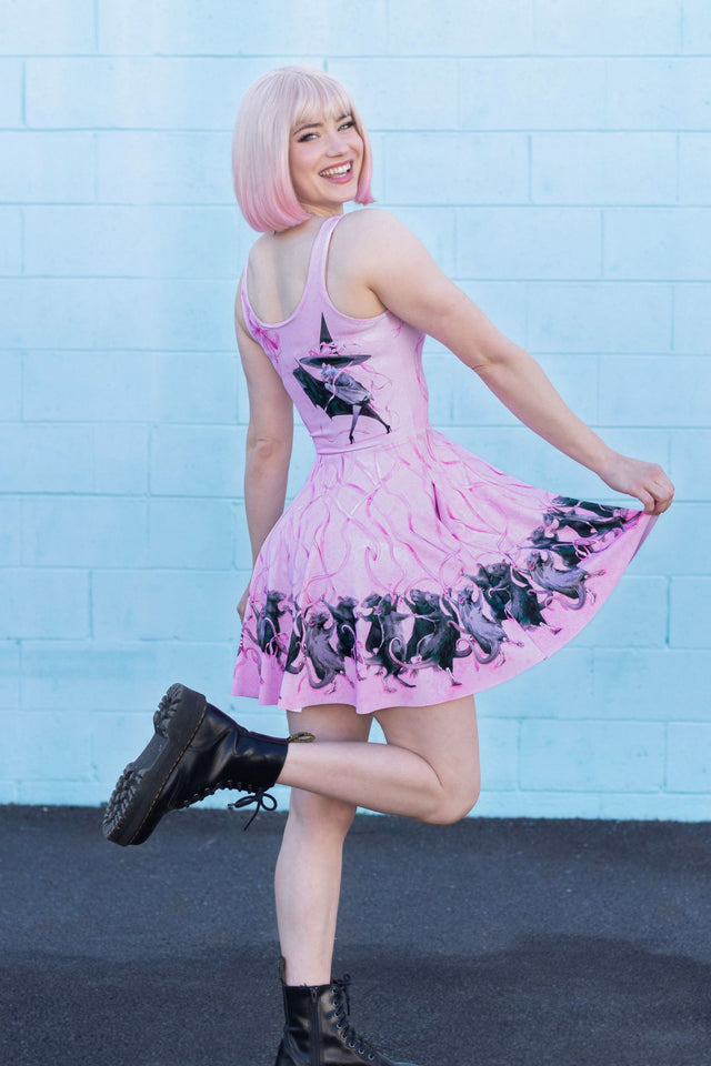 Woman wearing a pink dress with black patterns against a light blue brick wall.