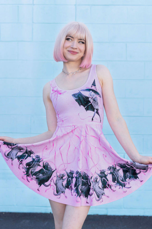 Woman wearing a pink dress with black graphics against a light blue tiled wall.