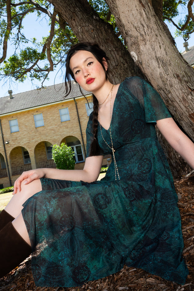 Dark green printed handkerchief dress with flutter sleeves, layered semi sheer skirt, uneven hemline and Celtic inspired design for romantic statement dressing
