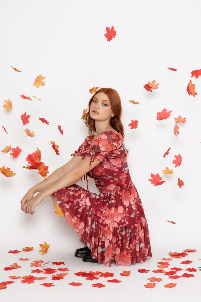 Woman in a red floral dress sitting on the floor with autumn leaves around her on a white background