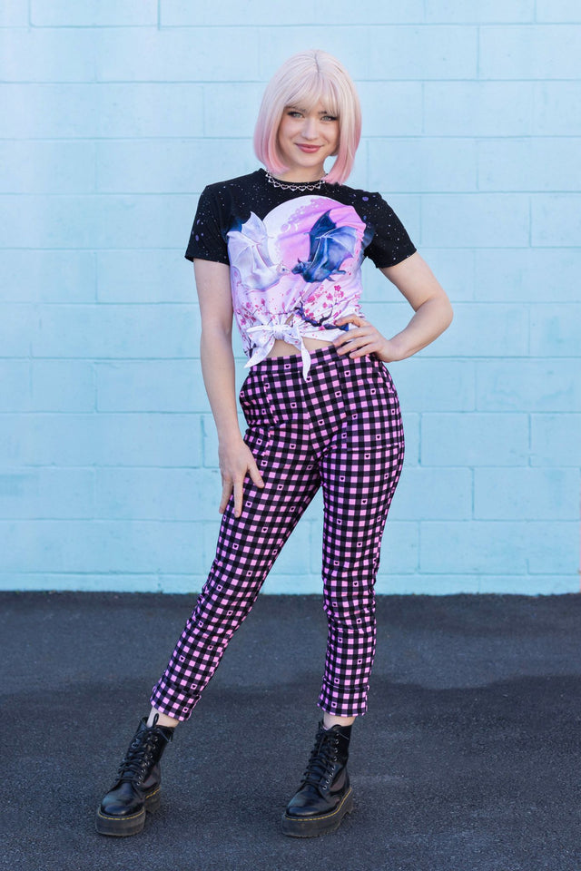 Person wearing a black t-shirt with a colorful design and purple checkered pants against a blue wall.