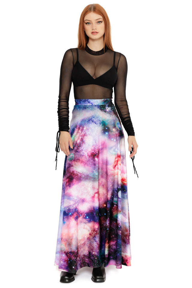 Model wearing a sheer black mesh long sleeve top with a flowing galaxy print maxi skirt in pink, purple and blue tones