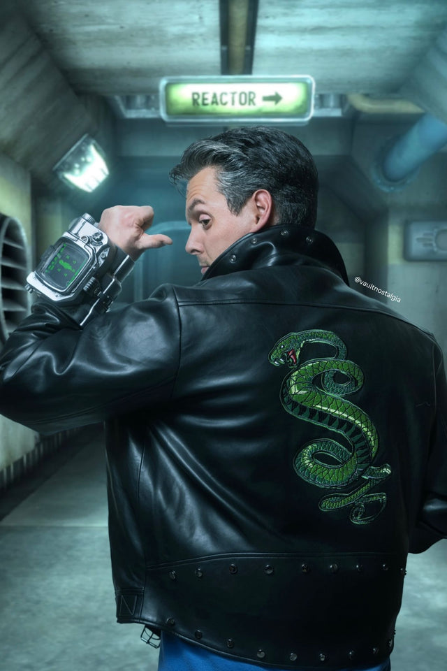 Person in a black leather jacket with a snake emblem, holding a device in a sci-fi corridor. Fallout