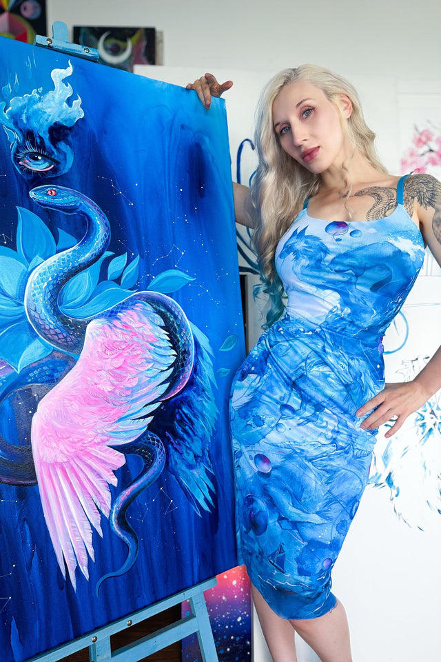 Woman wearing a blue dress with a dragon design, standing next to a painting of a dragon and pink creature.