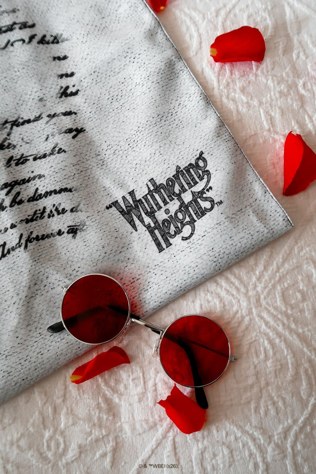 Gothic Drive Me Mad Tote Bag from the Wuthering Heights collection, shown in a romantic flatlay with roses and gift wrapping, featuring black shoulder straps and scripted text design