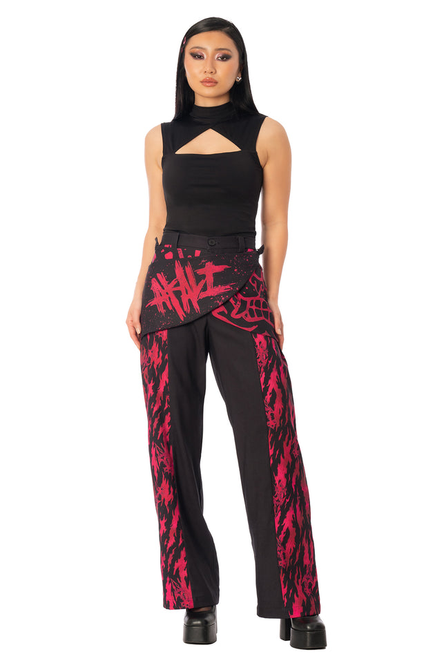 Model wearing black and red printed wide-leg drape pants with a black crop top. League of Legends K/DA x BlackMilk flowing black drape pants with red and pink Akali-inspired graphic print.