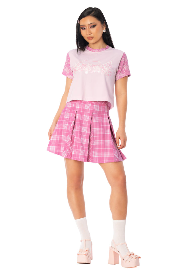Model wearing the pink baby tee with a pink plaid mini skirt. League of Legends K/DA x BlackMilk fitted pale pink cotton baby tee with pink sleeves and K/DA character symbols on the front.