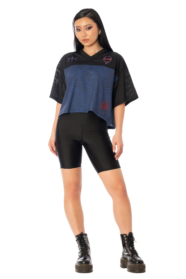 Model wearing the oversized cropped sports top with black bike shorts. League of Legends K/DA x BlackMilk oversized cropped sports-style touchdown top with Kai’Sa-inspired K/DA graphics.