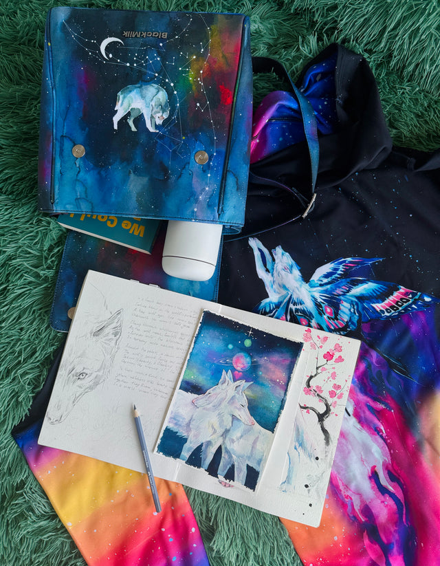 Artistic items including a notebook with drawings, a bottle of lotion, and a colorful fabric on a textured surface.